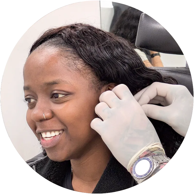 A smiling client having their ear jewellery changed by a piercer wearing white gloves