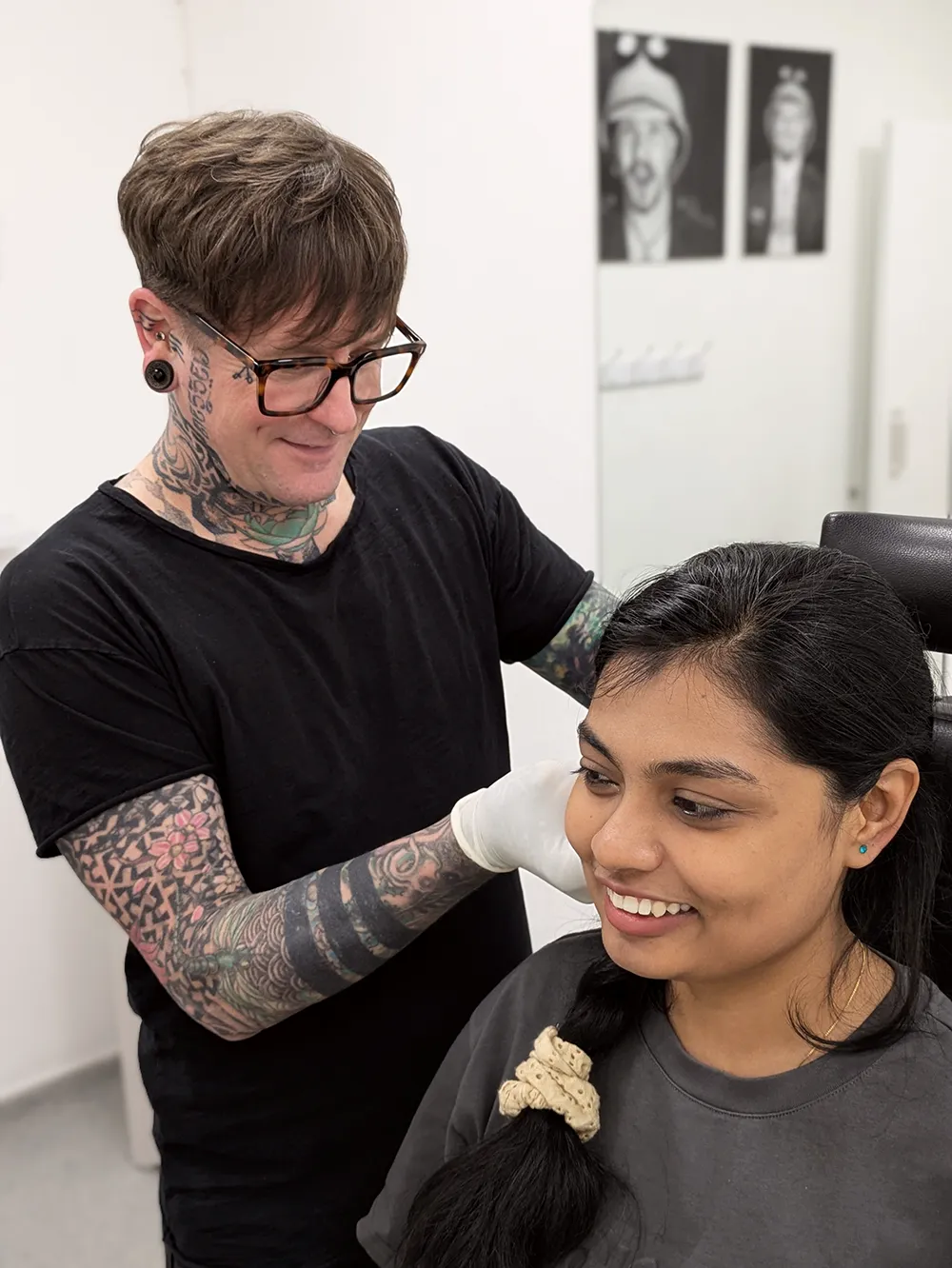 A smiling piercer fitting jewellery into a smiling clients ear at Metal Fatigue Piering in Bournemouth