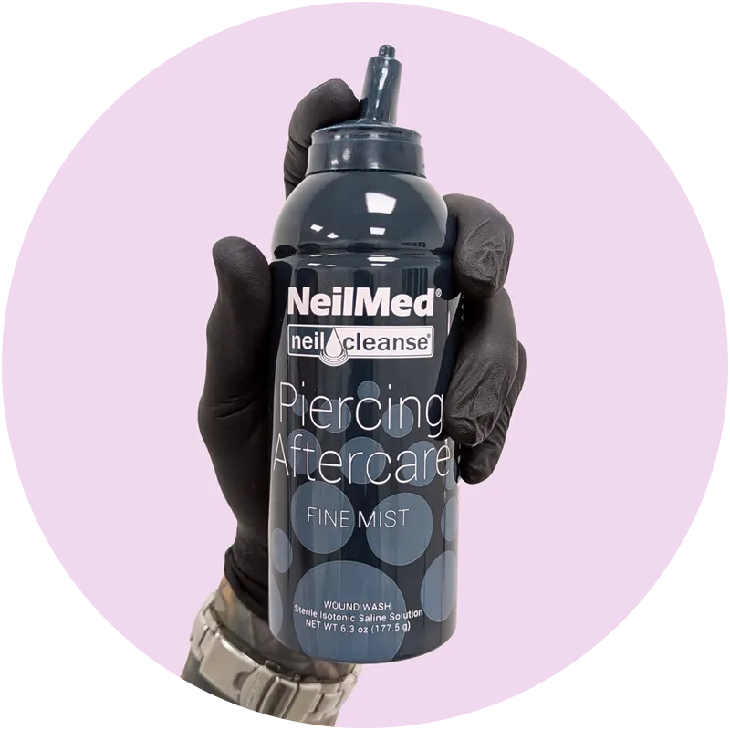 Close up a a gloved hand holding a can of NeilMed piercing aftercare spray