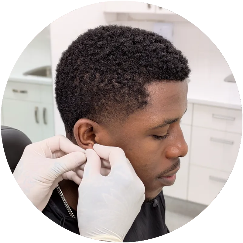 A client having their ear piercing jewellery changed by gloved hands