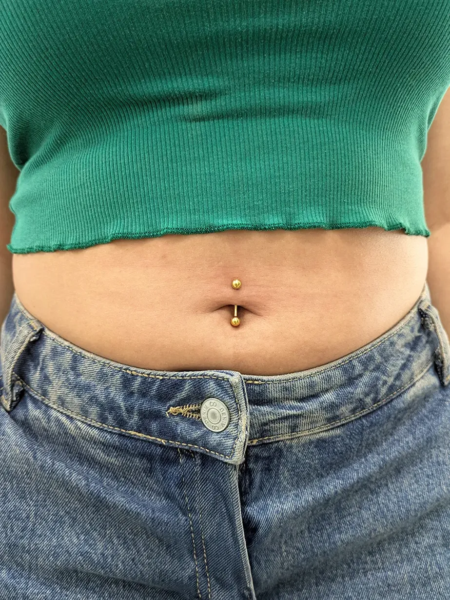 Close up of a woman with green top and jeans with a belly button piercing