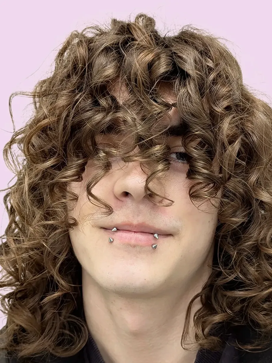 Man with long curly hair covering his eyes and a snakebites piercing