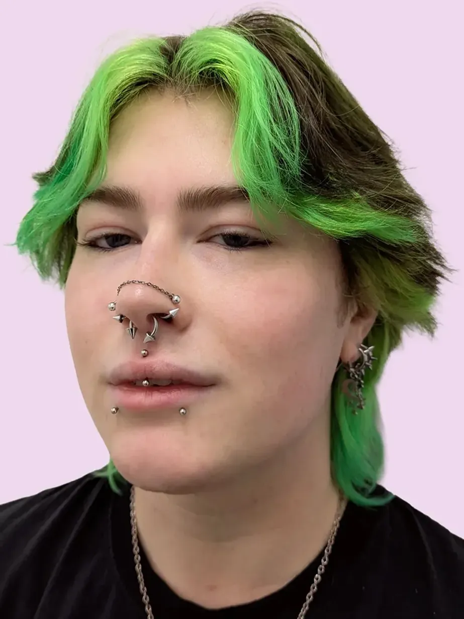 Portrait of a person with green hair and multiple facial piercings, including a septum and labret piercings