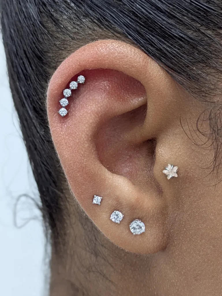 Close up of an ear with a crescent set helix piercing, earlobe piercings and a tragus piercing