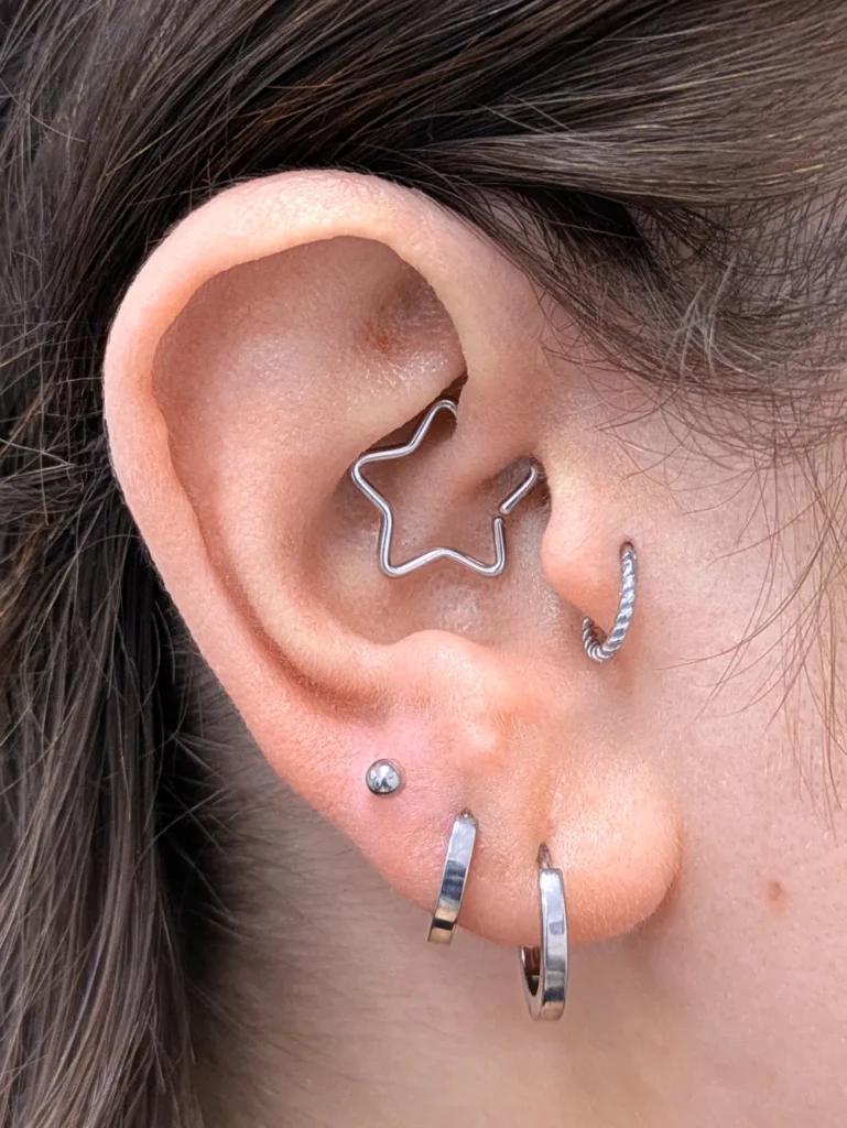 Close up of an ear with a daith piercing with a star shaped ring and tragus and earlobe rings