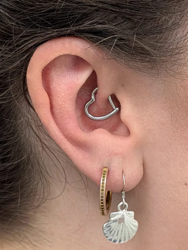 Close up of an ear with a heart shaped, gem set daith ring and earlobe piercings
