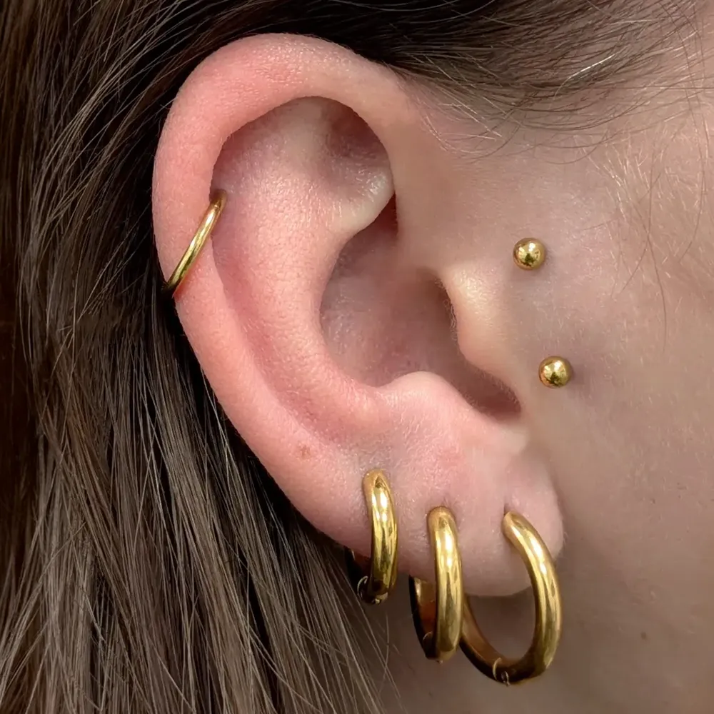 Close up of an ear with an anti-tragus piercing, earlobe piercings and a helix piercing