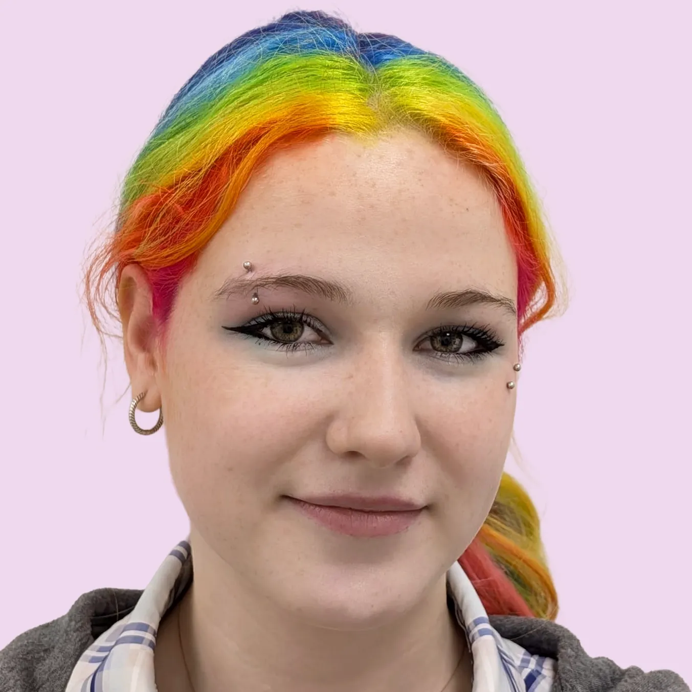 Person with rainbow coloured hair and a new anti-eyebrow piercing and an eyebrow piercing on the opposite side of their face